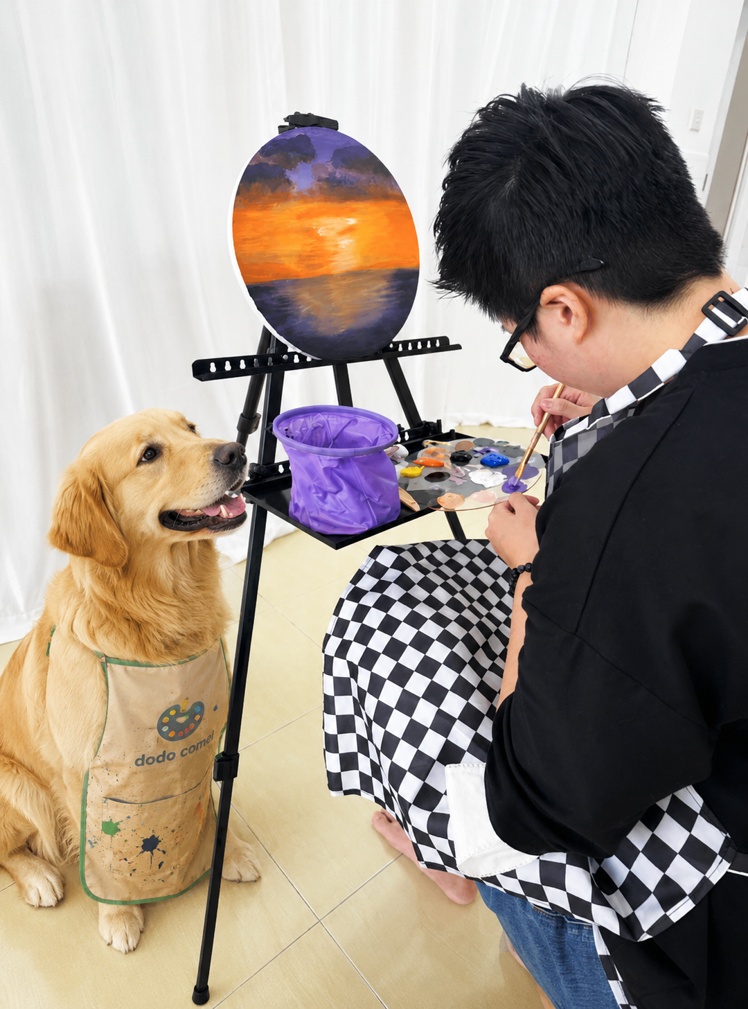 A small dog sitting next to paint brushes and an easel in an art studio